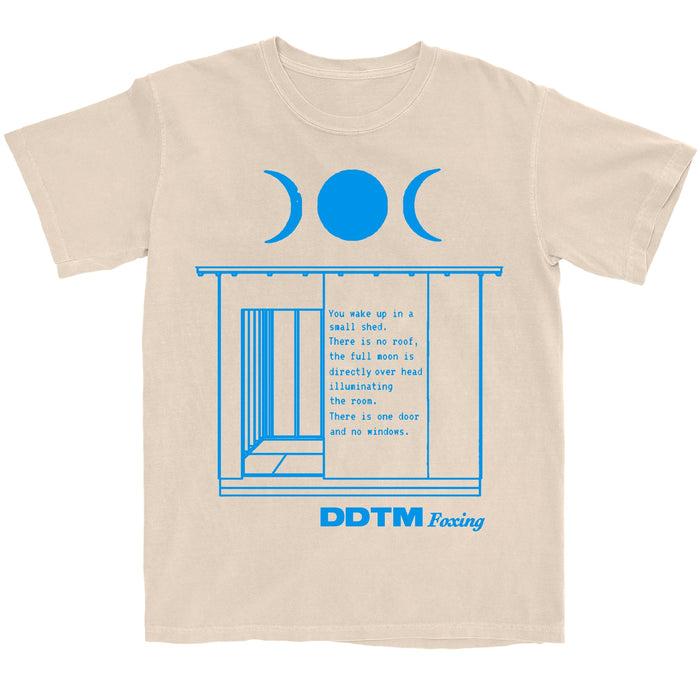 Ivory t-shirt on a white background. Top shows 3 phases of the moon in blue print. Bottom has text DDTM Foxing in blue print. In between if a shed w/ text.