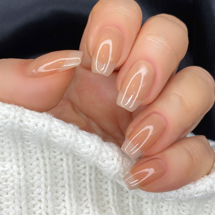 Beloved sheer nude brown nail polish close-up on a light skin tone with a white sweater