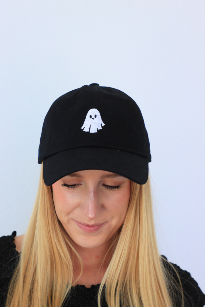 Person wearing a black cap with a ghost emoji on a light blue background