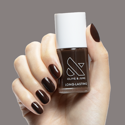 Hand with Dark Chocolate long-lasting nail polish by Olive & June on short rounded nails against neutral background