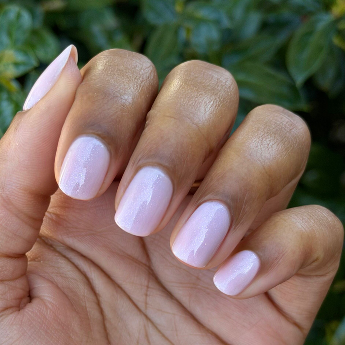 Hand with short nails painted in FIRST DATE milky strawberry pink polish with subtle silver glitter manicure