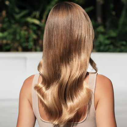 Woman with long, glossy, wavy blonde hair sitting outdoors.
