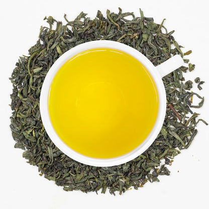 A cup of freshly brewed Organic China Green tea, surrounded by tea leaves.