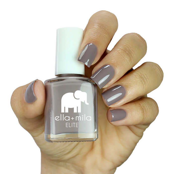 Traveler taupe purple nail polish on a medium skin tone, hand holding the bottle